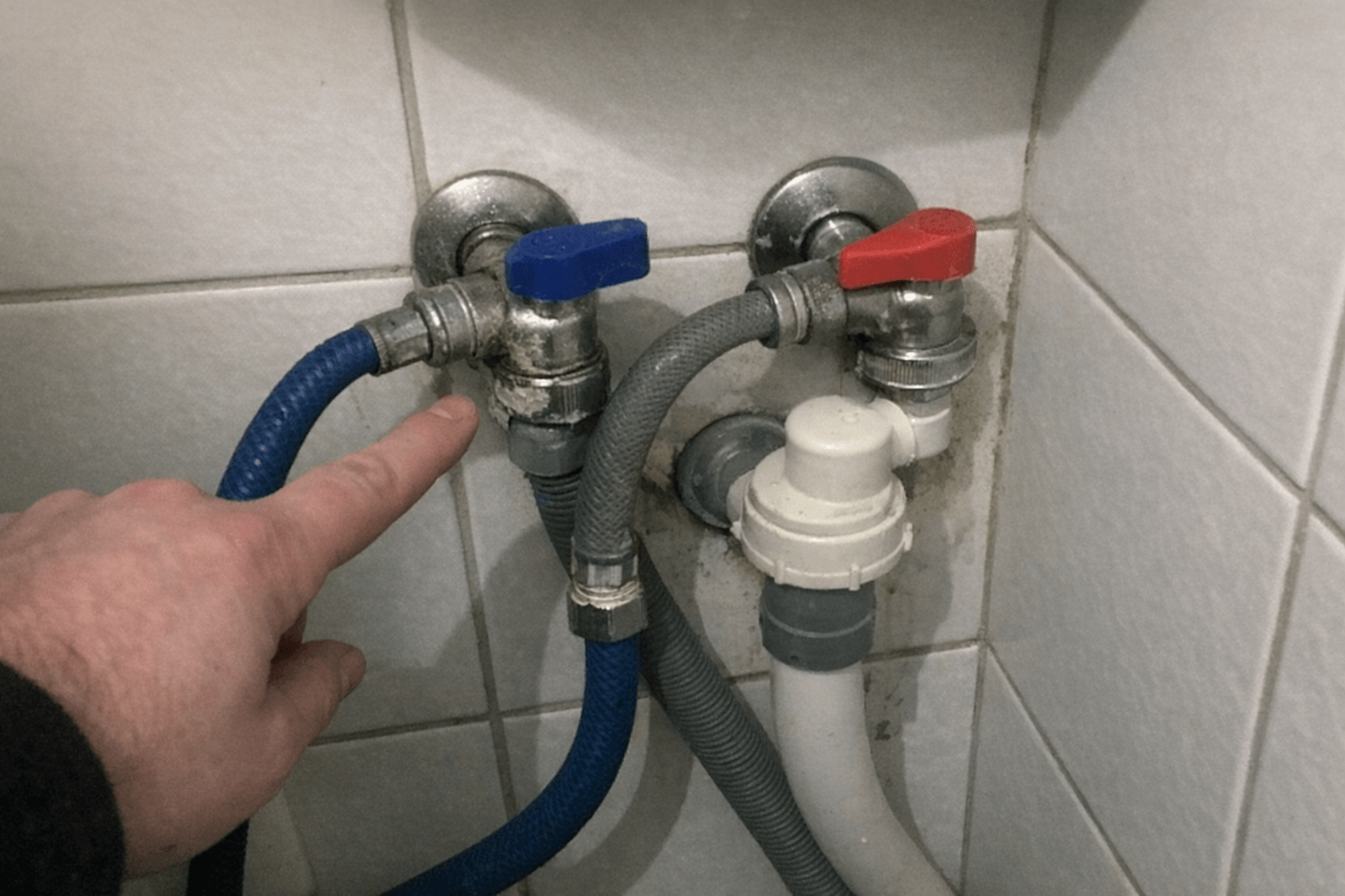 Hand mit Taschenlampe prüft Schlauchschellen am Ablauf hinter der Waschmaschine